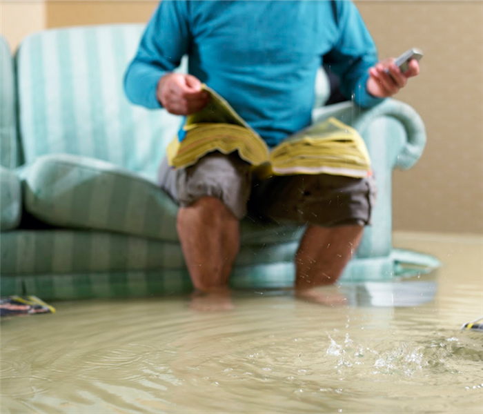 a man sitting on a couch in a flooded living room while using the phone book to make a call